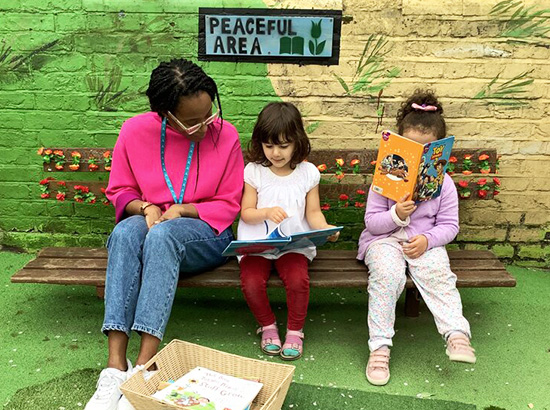 play worker helping nursery children read in term time